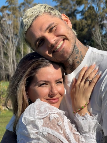 Un hombre de cabello rubio y tatuajes en el cuello apoya su cabeza junto a una mujer con vestimenta blanca de encaje en un entorno al aire libre
