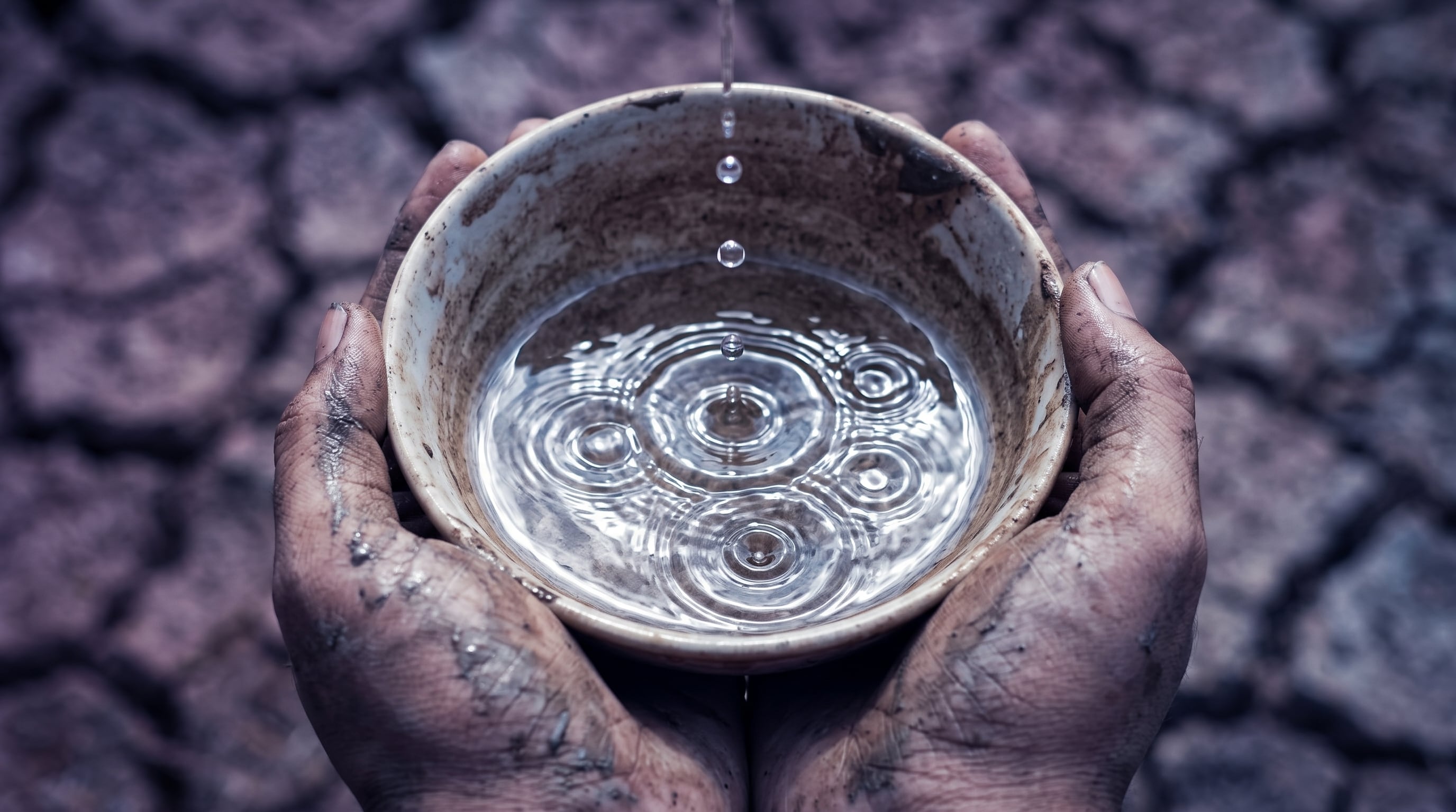 Unas manos manchadas de barro sostienen un cuenco que recibe gotas de agua sobre un suelo árido y agrietado por la sequía. (Imagen Ilustrativa Infobae)
