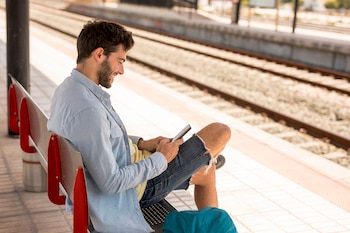 Un hombre mirando el móvil mientras espera al tren en una estación.