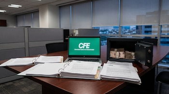 Un escritorio de madera con un portátil encendido que muestra el logo de CFE, documentos con el logo de CFE y una caja fuerte abierta con fajos de billetes.