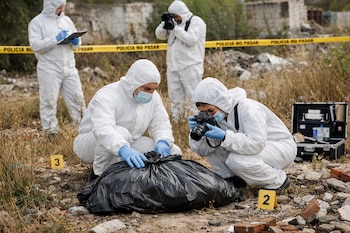 Cuatro personas con trajes blancos, mascarillas y guantes azules, una bolsa negra en el suelo, cámara de fotos, portapapeles, cinta "POLICIA NO PASAR".