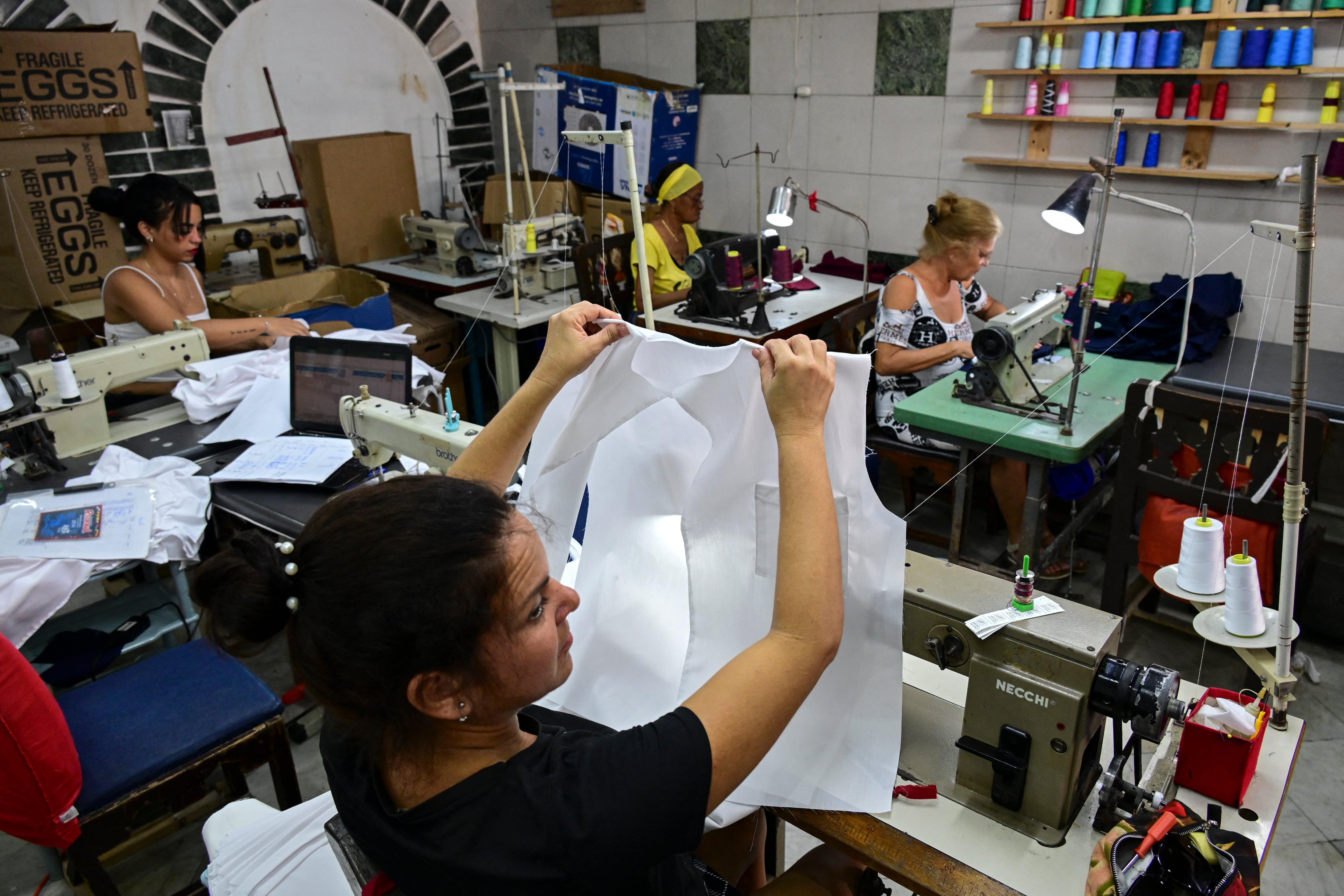 En las maquilas de uniformes, los pocos lapsos del día donde no hay apagones, aprovechan a elaborar la mayor cantidad de uniformes posible para suplir la demanda. (Photo by YAMIL LAGE / AFP)