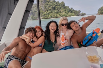 Cinco personas jóvenes, tres mujeres y dos hombres, sonríen en un barco. Una mujer rubia sostiene una pistola de agua naranja y un hombre una azul