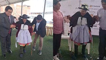 Una mujer anciana con sombrero tradicional y falda plisada es asistida por dos hombres mientras camina sobre un césped artificial bajo un techo blanco