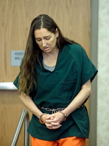 Megan Huntsman, con cabello largo y castaño, viste uniforme de prisión verde y pantalones naranjas, con las manos esposadas y la cabeza inclinada