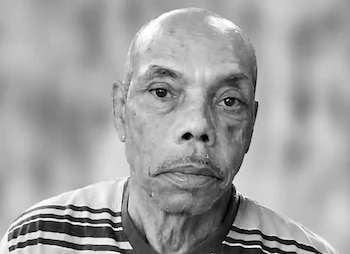 Retrato en blanco y negro de un hombre mayor con camiseta a rayas frente a un fondo desenfocado