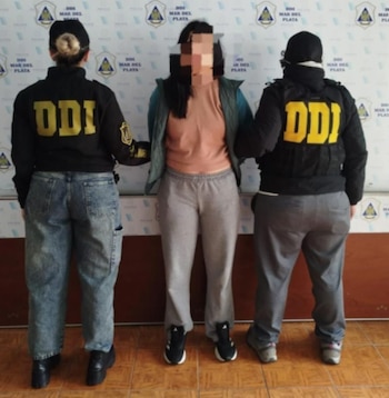 Dos agentes con indumentaria de la DDI escoltan a una mujer con el rostro pixelado frente a un panel con logotipos oficiales