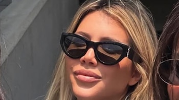 Primer plano de una mujer con cabello rubio y gafas de sol negras, parte de otra persona visible a la derecha