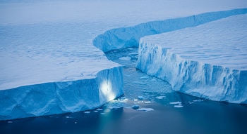 Vista aérea de la capa de hielo de Groenlandia dividida por profundas grietas, con ríos de agua azul intensa y trozos de hielo flotando entre los bloques.