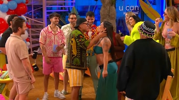 Un grupo de diez personas en un evento festivo; un hombre con camisa estampada abraza a una mujer de cabello largo; globos rojos, azules y blancos de fondo