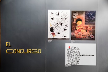 Panel de exposición oscuro con texto amarillo 'EL CONCURSO' y tres ilustraciones enmarcadas: una con pájaros, una niña con juguetes, y un paisaje abstracto con casas