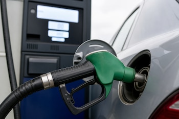Boquilla verde de un surtidor de combustible introducida en el tanque de un automóvil gris.