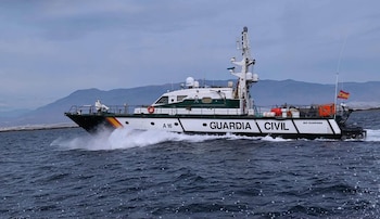 Una patrullera blanca y verde con el rótulo Guardia Civil navega en el mar con montañas al fondo