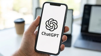 Una mano sostiene un teléfono inteligente mostrando el logo de ChatGPT y su nombre en una pantalla blanca, con un fondo difuminado.