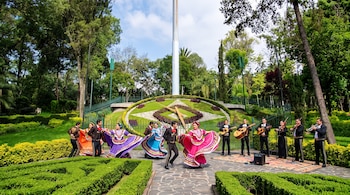 Bailarines con vestidos folclóricos y músicos de mariachi realizan una danza frente a un gran reloj floral.