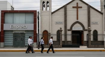 Cuatro personas caminan por una calle junto a un edificio con cartel "Empresa" y una iglesia con cruz, campanario y letreros "IGLESIA", "SÁBADO DE CULTO".