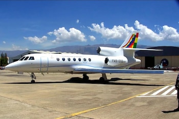 Avión blanco con la inscripción FAB-002 y la bandera wiphala en la cola, estacionado en una pista bajo un cielo despejado
