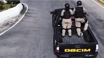 Vista superior de dos personas con casco y uniforme militar en la caja de una camioneta negra con la inscripción DGCIM