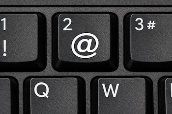 Primer plano de una tecla negra de un teclado con el número '2' y el símbolo blanco de arroba '@' impresos claramente.