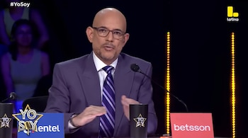 Ricardo Morán, un hombre calvo con gafas y traje morado, sentado en un panel de televisión con el logo "Yo Soy" y "Latina" visibles