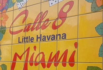 Mural de azulejos amarillo brillante con las palabras 'Calle 8' en rojo, 'Little Havana' en azul y 'Miami' en rojo, rodeado de flores y dominós
