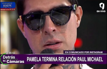 Primer plano de Paul Michael con gafas de sol oscuras y tatuajes en el cuello, sosteniendo un micrófono mientras habla en una entrevista televisiva