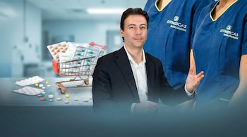 Daniel Quintero en traje oscuro con gesto de mano, carrito con envases de medicamentos a la izquierda y píldoras esparcidas. Personal de Offimédicas en uniformes azules al fondo.