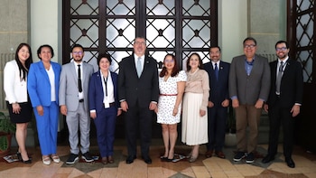 Nueve personas, cinco mujeres y cuatro hombres, posan sonriendo de pie frente a unas grandes puertas de madera ornamentadas