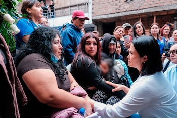 Keiko Fujimori, vestida de blanco, conversa con un grupo de mujeres y hombres; un niño aparece difuminado en el centro. Al fondo, un edificio de ladrillos