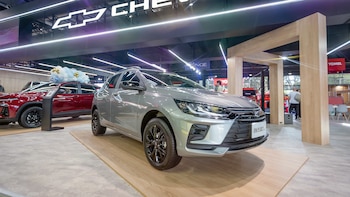 Un SUV Chevrolet Onix Activ gris en primer plano y un SUV Chevrolet rojo con globos en segundo plano. Ambos están sobre plataformas de madera, con un cartel luminoso de Chevrolet