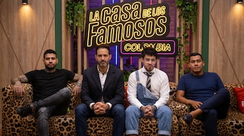 Cuatro hombres sentados en un sofá de estampado de leopardo. Al fondo, un gran logo de neón con 'La Casa de los Famosos Colombia' ilumina el set.