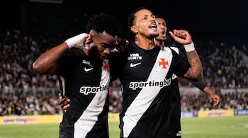 Tres futbolistas con la camiseta negra y franja blanca del Vasco da Gama celebran en la cancha con los puños en alto.