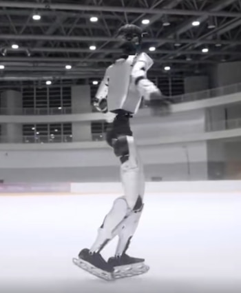 Un robot humanoide de color blanco y negro, con patines de hielo, se desliza sobre una pista de hielo cubierta con luces en el techo