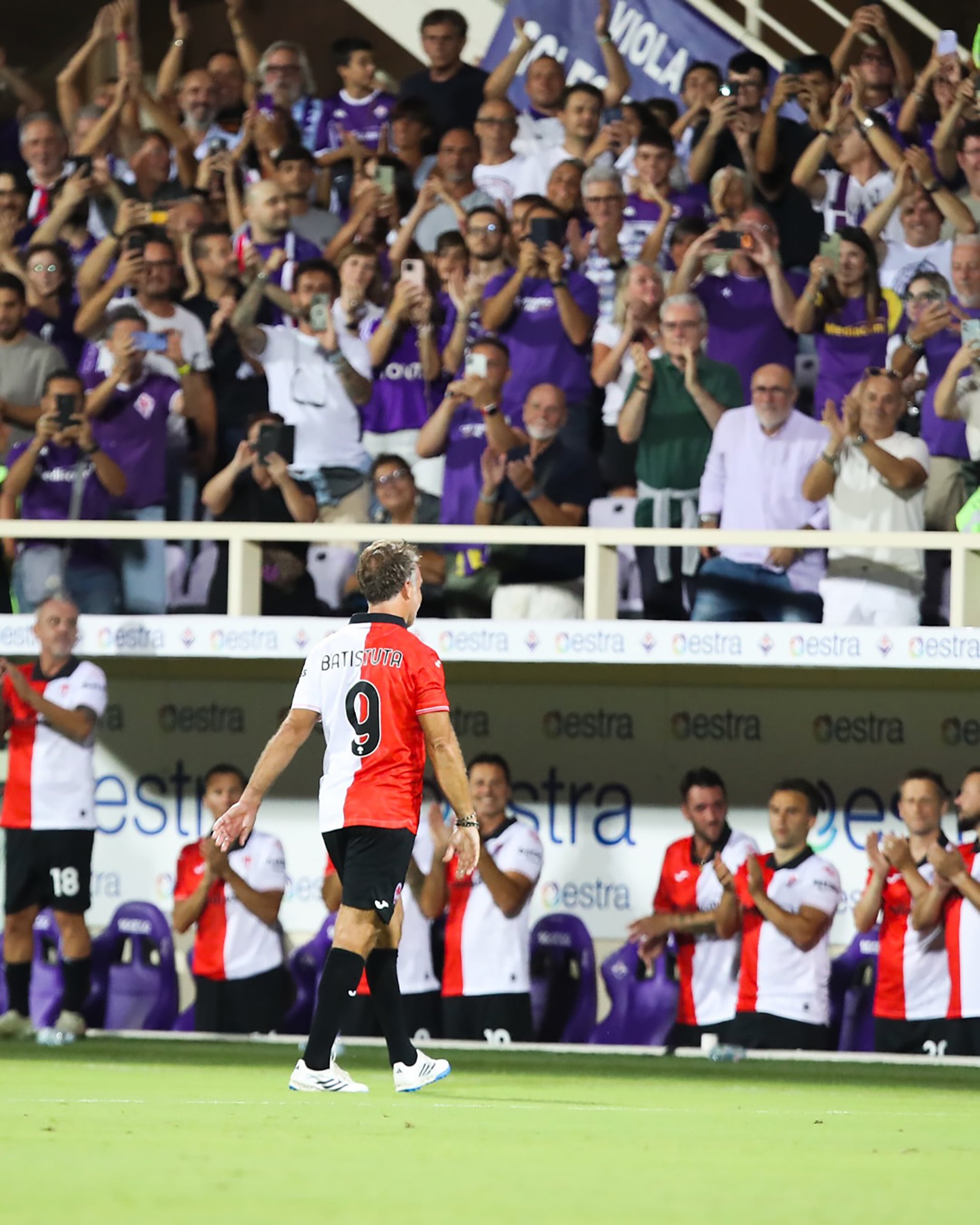 Gabriel Batistuta camina por el terreno de juego con la camiseta número nueve mientras los espectadores en la tribuna lo aplauden.