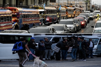 Autobuses y automóviles alineados en la parte superior y varias personas de pie junto a furgonetas blancas en la parte inferior.
