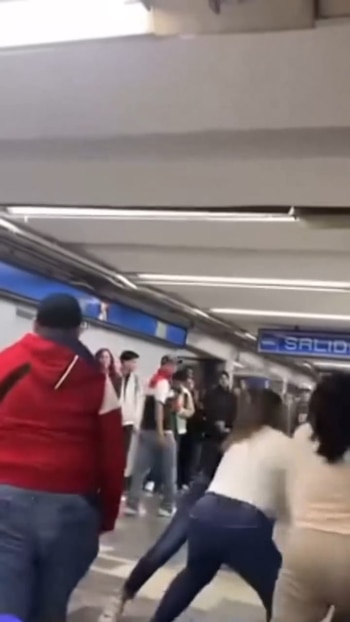 Varias personas en una estación de metro. Al fondo se observa un letrero luminoso con la palabra SALIDA. Una persona con sudadera roja y dos mujeres en jeans son visibles