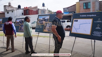 Tres hombres observan paneles informativos en la calle. Un panel muestra un mapa con la ruta del Trolebús Ixtapaluca