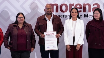 Un hombre muestra un documento impreso junto a tres mujeres ante una pared con el logotipo del partido político Morena.