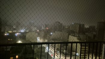 Una barandilla y red de seguridad en un balcón, con edificios e luces de una ciudad de noche al fondo