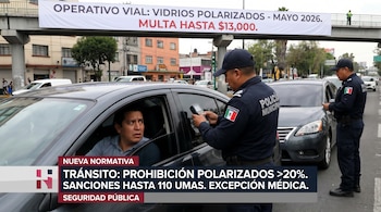Un policía municipal revisa a un conductor en un coche oscuro con la ventanilla abierta en una calle con tráfico; otro agente y un cartel de "Operativo Vial" son visibles.