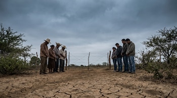 Tierra seca y agrietada en Nicaragua. Dos grupos de personas, uno con ropa tradicional y otro moderna, se miran a través de una cerca de alambre bajo cielo nublado.