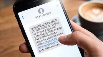 Mano de persona sostiene un teléfono móvil que muestra en pantalla un mensaje de texto con un aviso de suspensión de servicios.