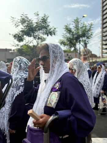 Mujeres vestidas con túnicas moradas y velos blancos de encaje avanzan por una calle al aire libre