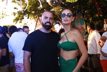 Brian Rullan, hombre barbudo con camiseta negra, y Laura Spoya, mujer con top y falda verdes y gafas de sol, posan en un evento nocturno