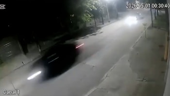 Cámara de seguridad nocturna muestra un coche oscuro con luces traseras y delanteras en movimiento en una carretera. Otro vehículo con faros se acerca en la distancia