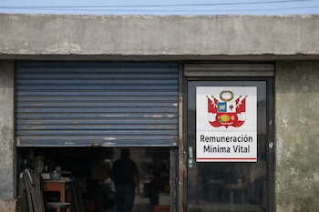 Fachada de una microempresa con persiana azul parcialmente bajada y una puerta de vidrio que exhibe un cartel con el escudo de Perú y el texto "Remuneración Mínima Vital".