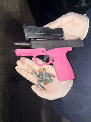 Persona con guantes blancos sostiene una pistola rosa con cargador negro y ocho balas con puntas doradas, sobre un fondo oscuro