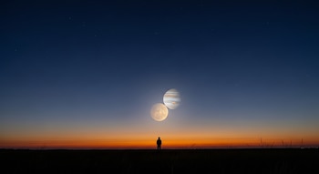 Silueta de una persona en un campo abierto al atardecer, observando los planetas Venus y Júpiter brillando intensamente y muy cerca en el cielo crepuscular.