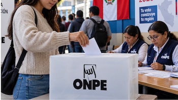 Una mujer deposita un papel en una urna con el logotipo de la ONPE frente a dos personas en una mesa y una bandera de Perú