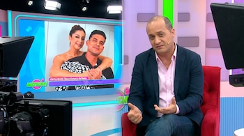 Un presentador de televisión calvo con chaqueta azul y camisa rosa sentado en una silla roja, con las manos extendidas, frente a una pantalla con una pareja.